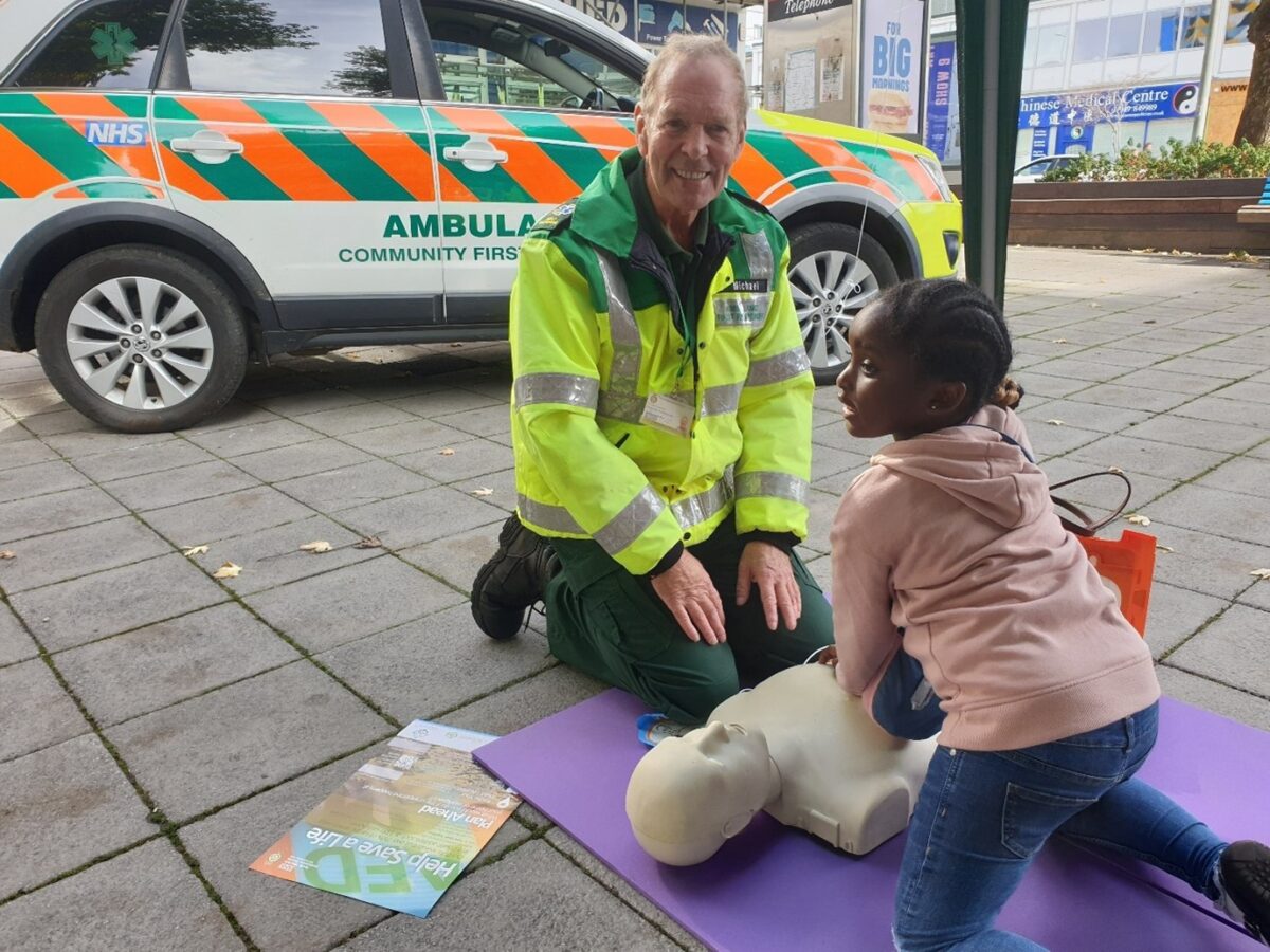 man in ambulance jacket teaching cpr to a child